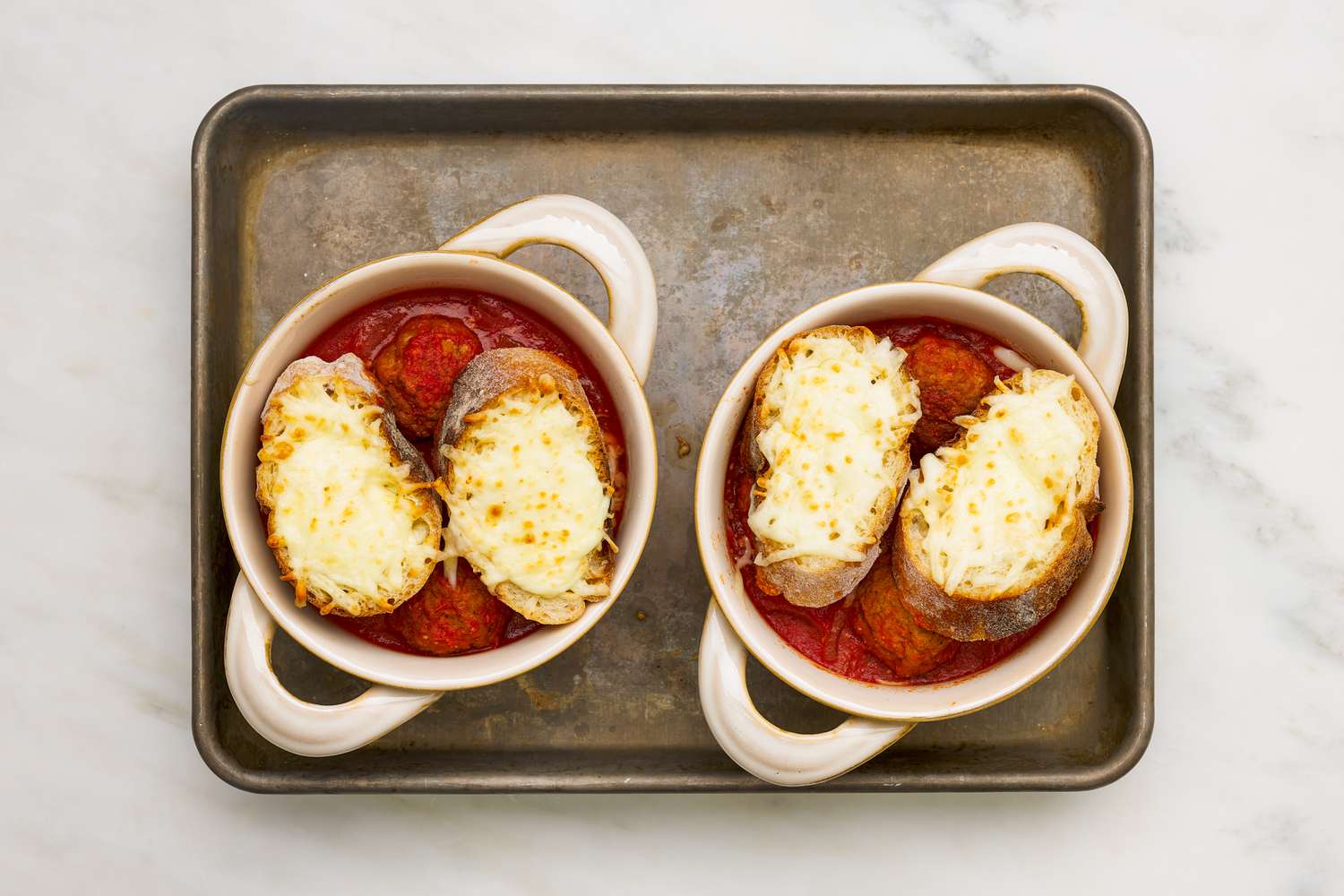 Meatball sub soup assembled in a pot-like ramekin, sitting on a baking tray 