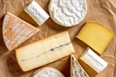 Various types of cheese arranged on brown parchment paper including soft and hard cheese varieties in multiple shapes and textures
