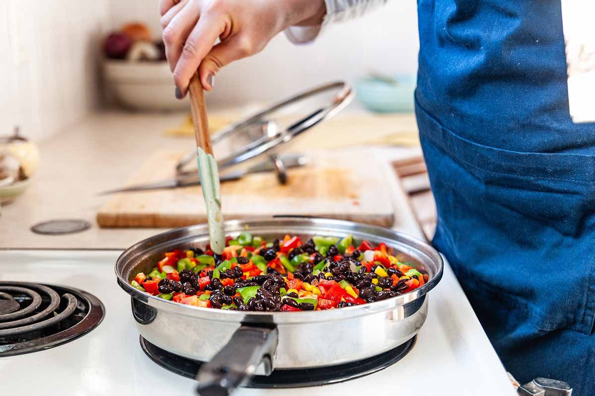 Chicken Recipe in Skillet with Cumin - womans hand stirring chicken and vegetables with spatula