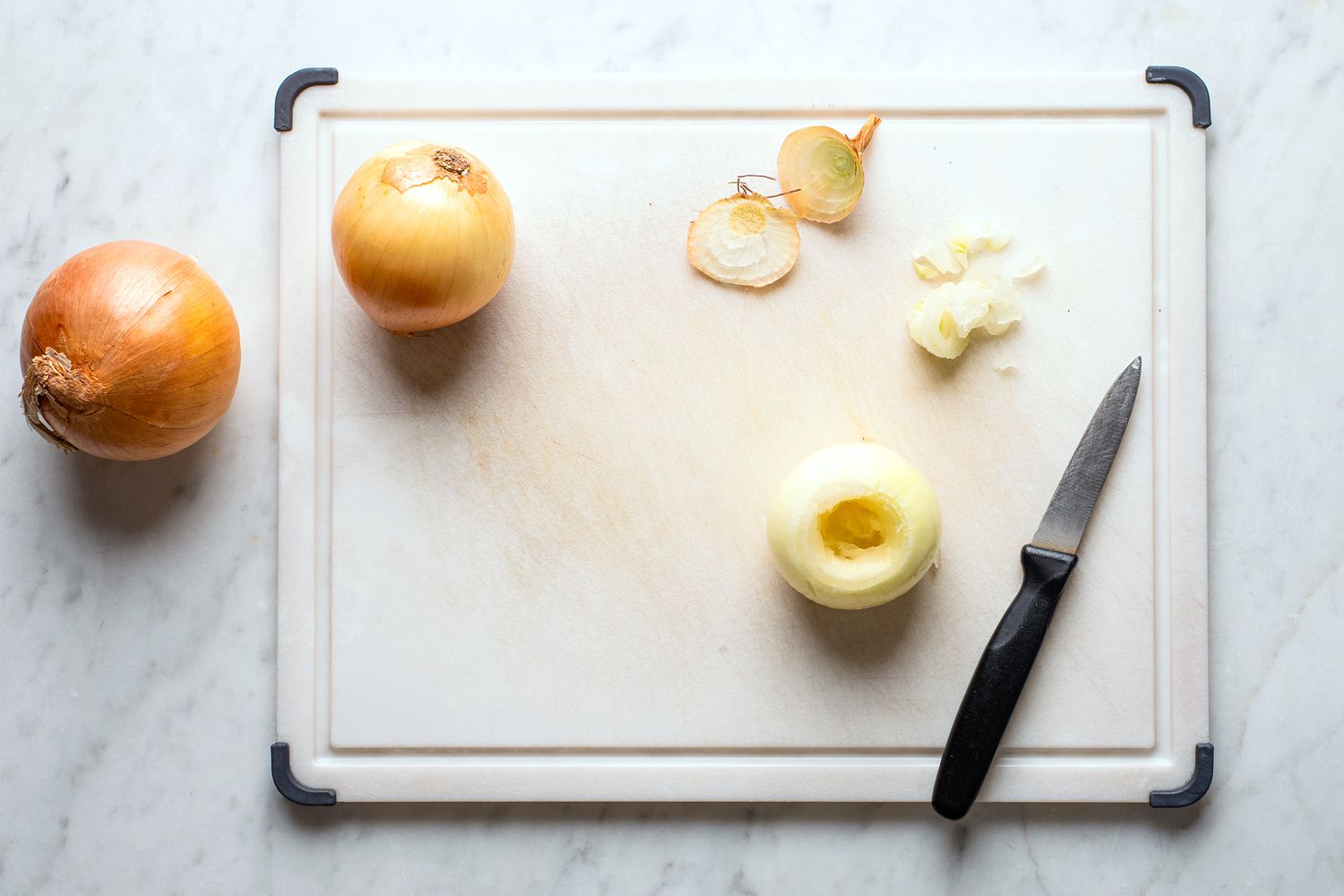 Three onions on a cutting board one partially peeled with a knife nearby