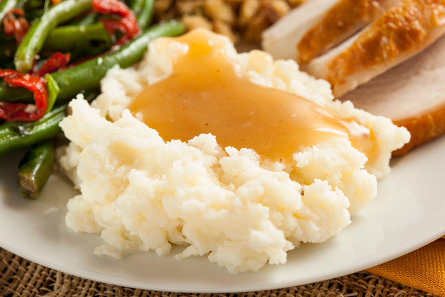Angled view of mashed potatoes and gravy next to green beans and turkey slices on a white plate