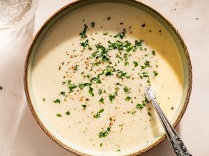 Bowl of cauliflower bisque garnished with chopped herbs and black pepper with a spoon placed inside