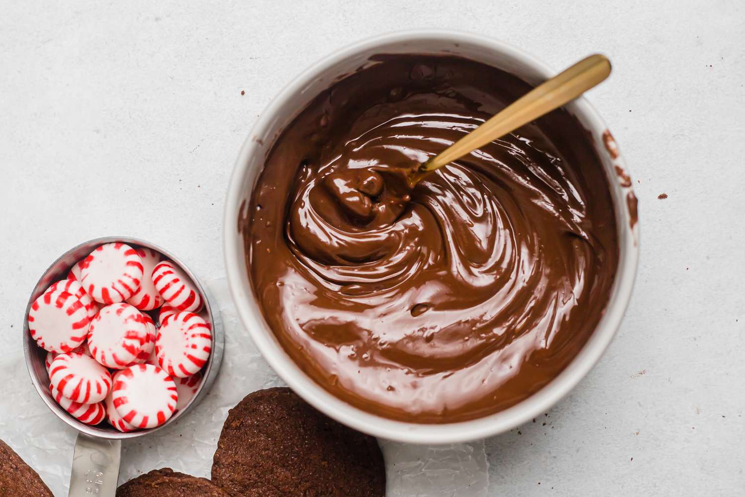 Melted chocolate in a metal bowl and a measuring cup of peppermints.