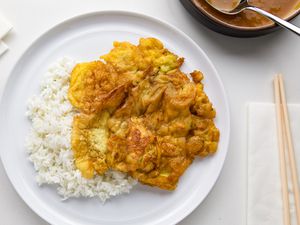 Egg Foo Young on a Plate with Jasmine Rice at a Table Setting with Chopsticks on a Napkin and a Pot of Sauce