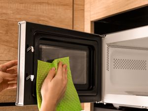 A person cleaning a microwave interior with a cloth
