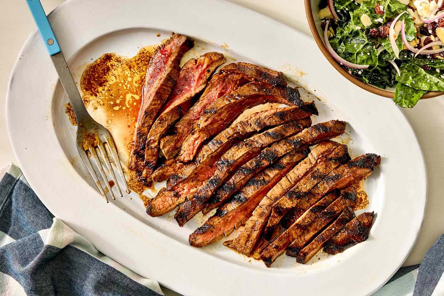 Sliced marinated flank steak on a serving platter with a fork on the side