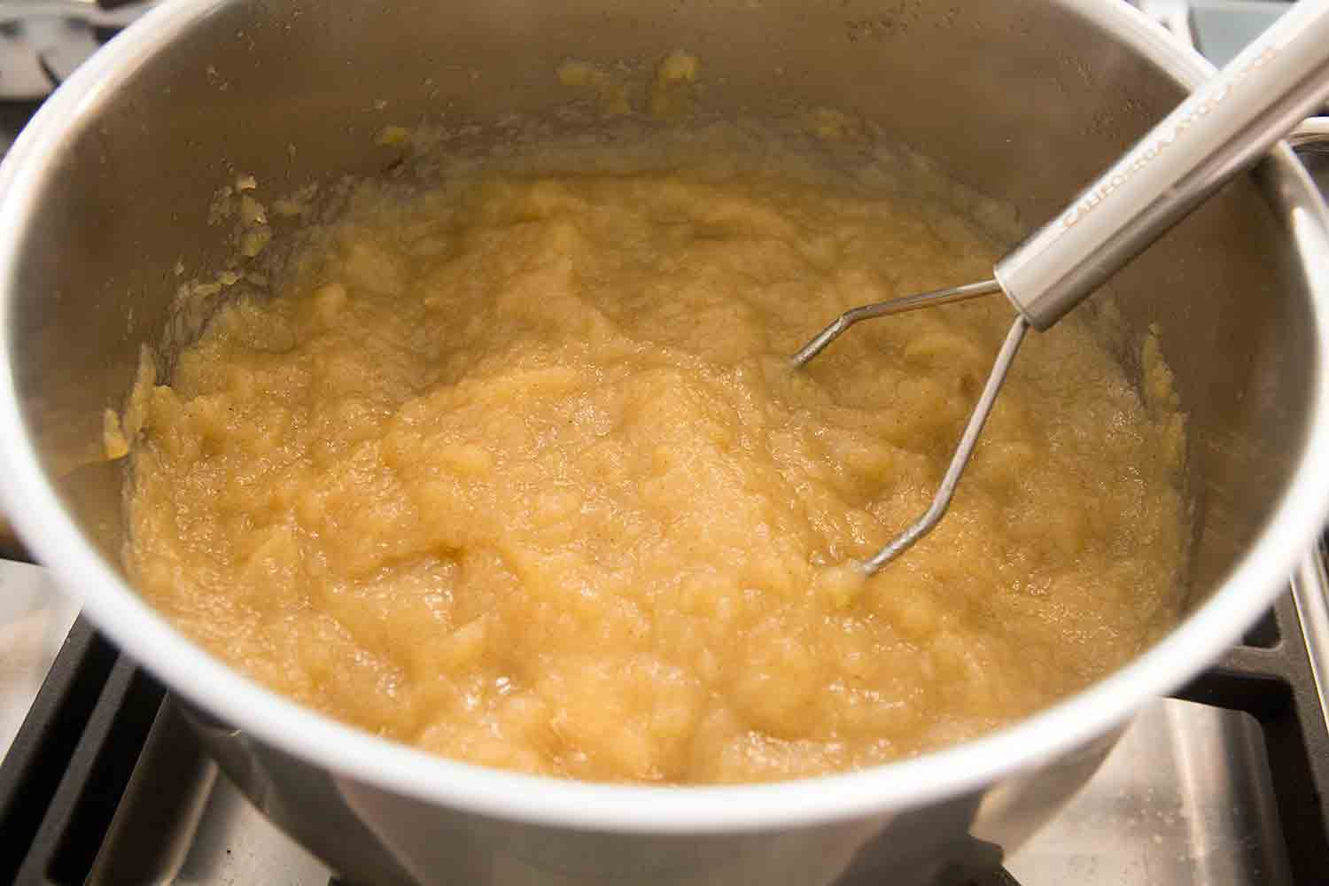 A pot of cooked applesauce with a masher in it