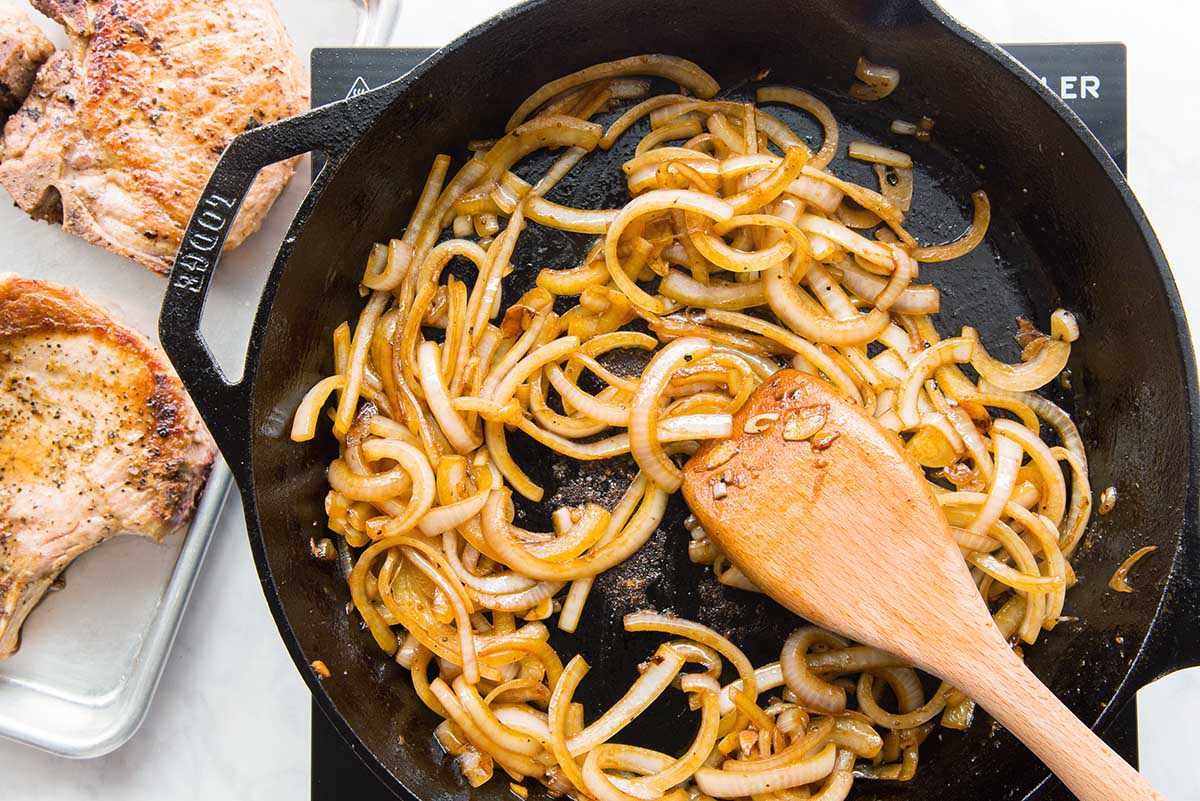 Onions sauteed in a cast iron skillet with a wooden spoon.