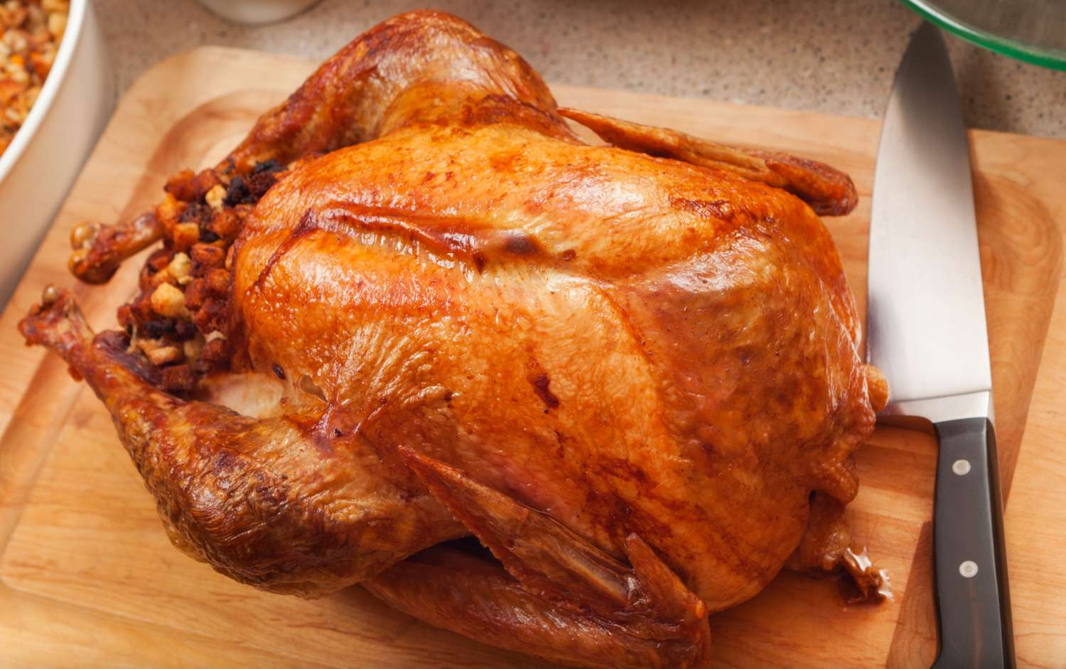 A whole roasted turkey on a wooden cutting board, with a chefs knife on the right side