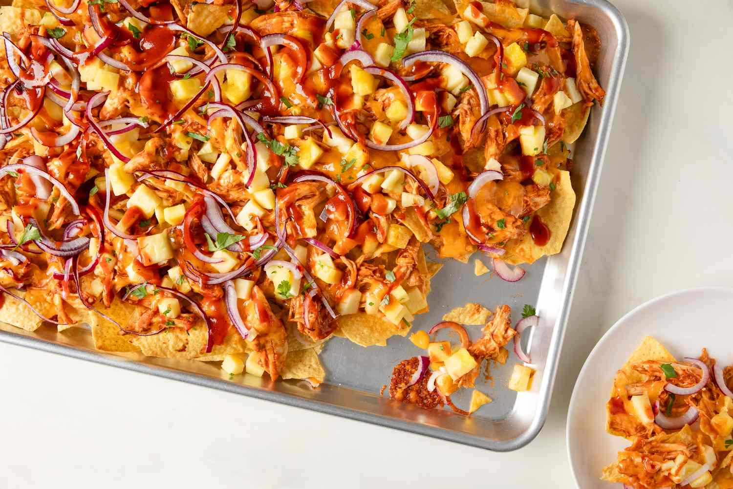 overhead view of a sheet-pan of BBQ Chicken Sheet Pan Nachos, a serving scooped out and on a small plate