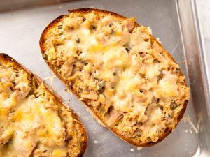 Toasted bread slices topped with a mixture of tuna and melted cheese on a baking tray