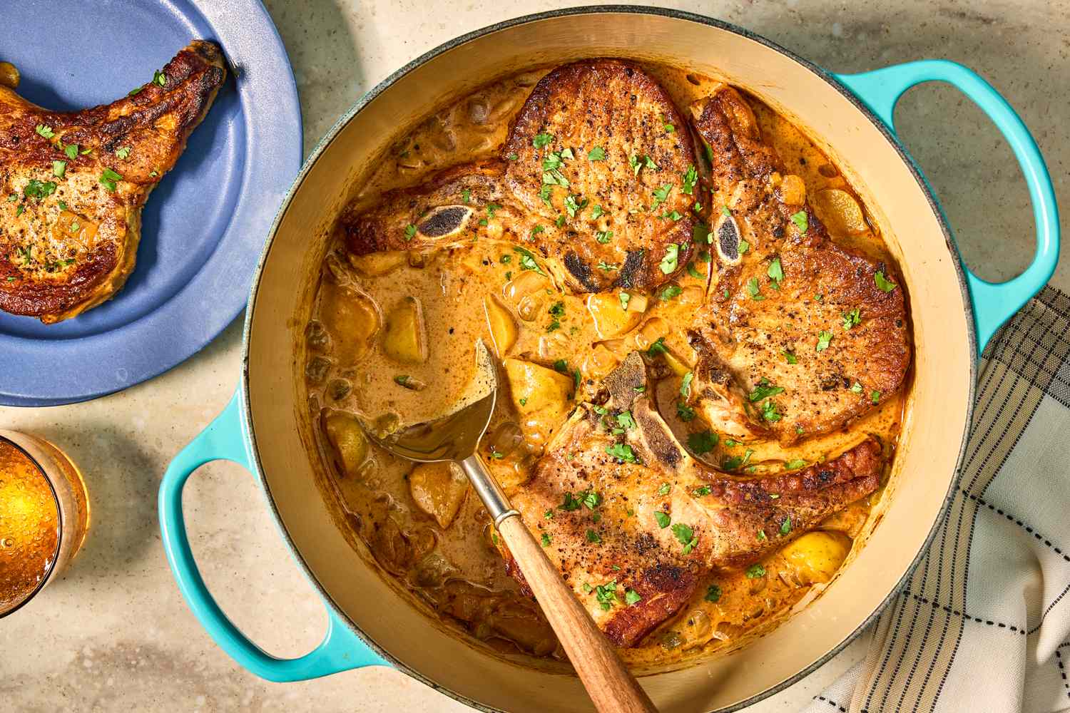 Cooked pork chops in a creamy sauce in a pot with a spoon served on a plate nearby