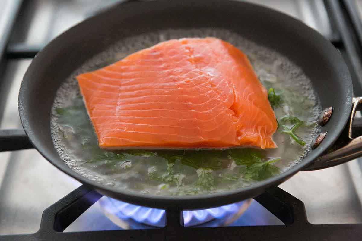 Salmon poaching on top of herbs in a pan on gas stove