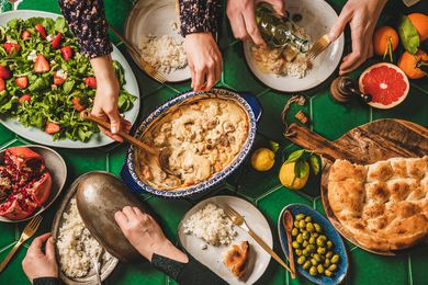Family having Turkish dinner. Flat-lay of hands serving and eating with lamb in yogurt sauce, fresh arugula and strawberry salad, rice pilaf and flatbread.