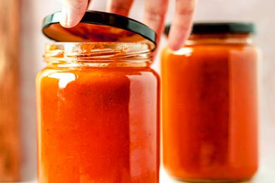 Jar of tomato sauce being opened by a hand another jar in the background