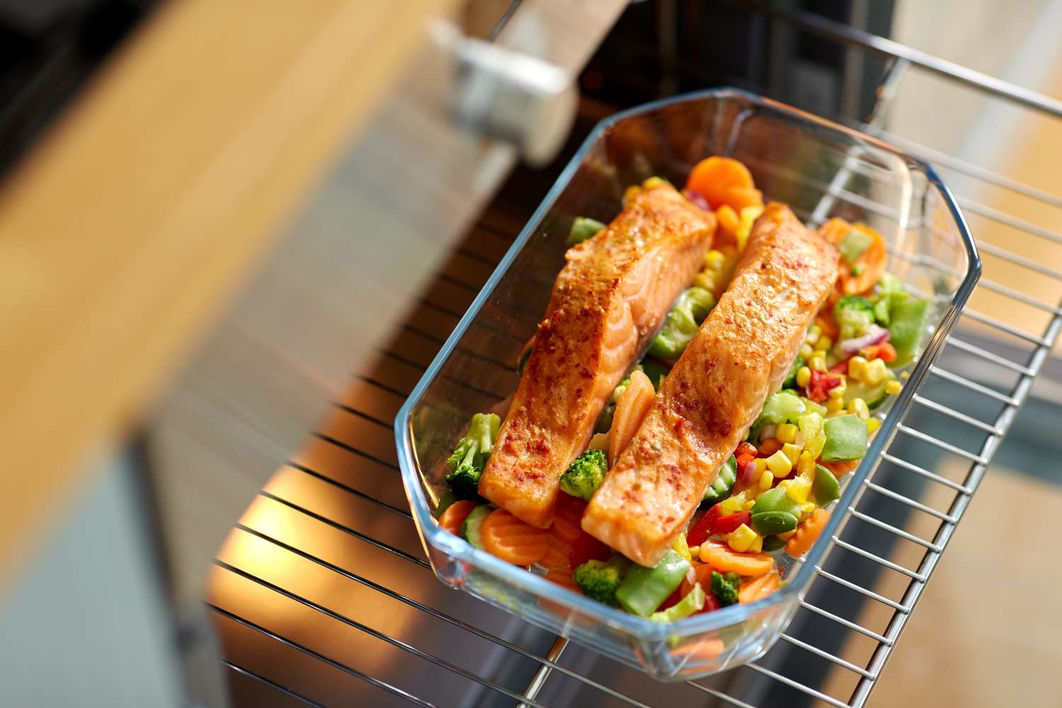 Salmon filets on top of roasted vegetables in a glass baking dish placed on an oven rack