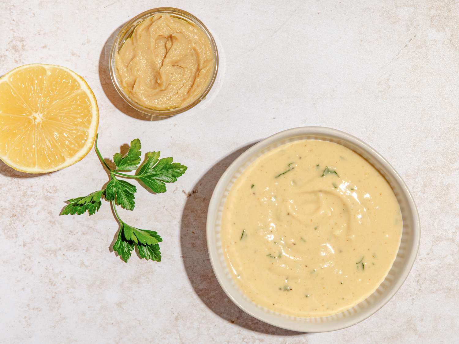 Bowl of hummus salad dressing, a halved lemon, a bowl of hummus, and parsley