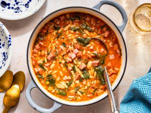 Swamp soup in a dutch oven at a table setting with bowls, a glass, utensils, and a kitchen towel