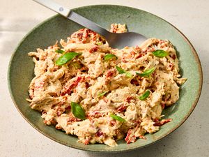 A bowl of chicken salad garnished with basil leaves, served with a spoon