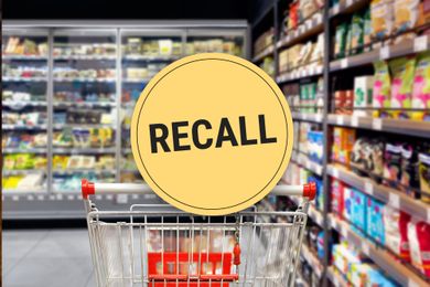 Shopping cart in a grocery store aisle with a large yellow recall sign displayed