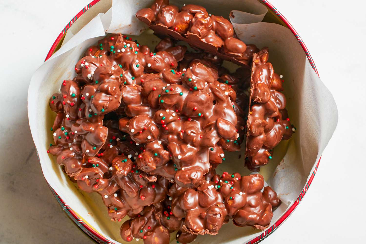 Chocolate candy clusters with nuts and sprinkles in a container lined with paper