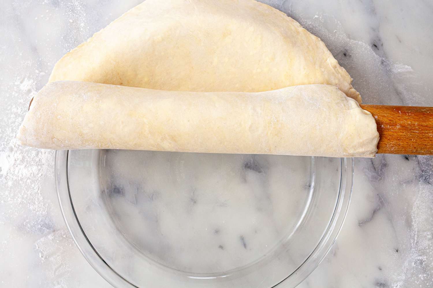 Using a rolling pin to place an easy pie crust in a glass pie plate.