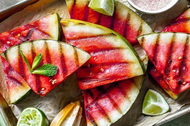 Triangles of grilled watermelon with small bowl of spice mix, sprig of mint and lime wedges alongside
