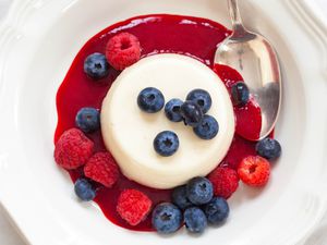 Panna Cotta with berries and sauce in a round bowl with a spoon.