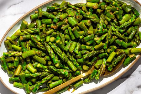 Sauteed asparagus pieces arranged on a platter with a serving spoon.