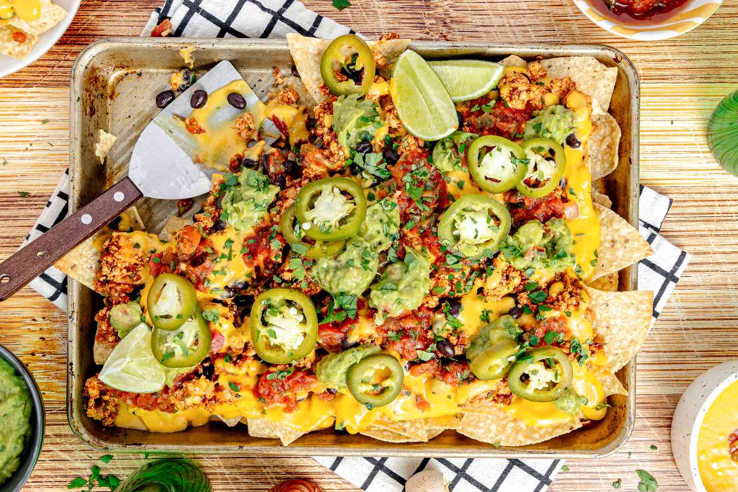 Baking Sheet of Vegan Nachos (Nachos Topped with Salsa, Queso, Pickled Jalpenos, and Two Lime Wedges) with a Serving Missing 
