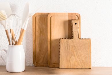 Wooden cutting boards propped against a wall next to a white ceramic container holding kitchen utensils