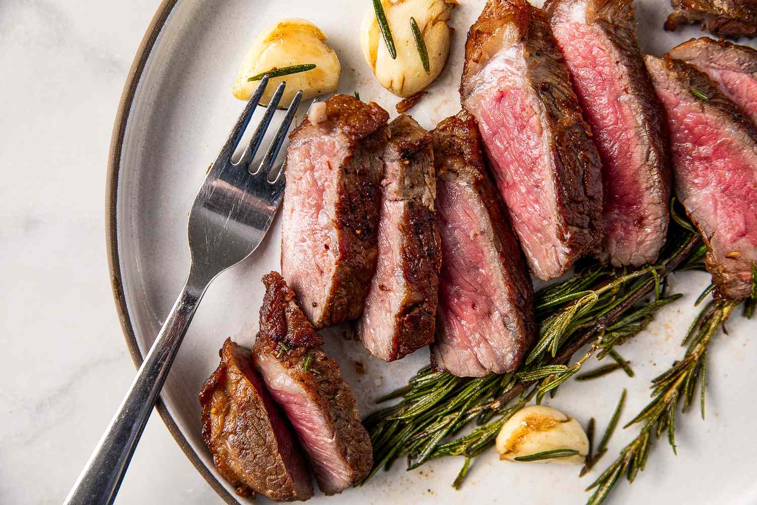 Sliced steak with garlic and rosemary on a plate with a fork