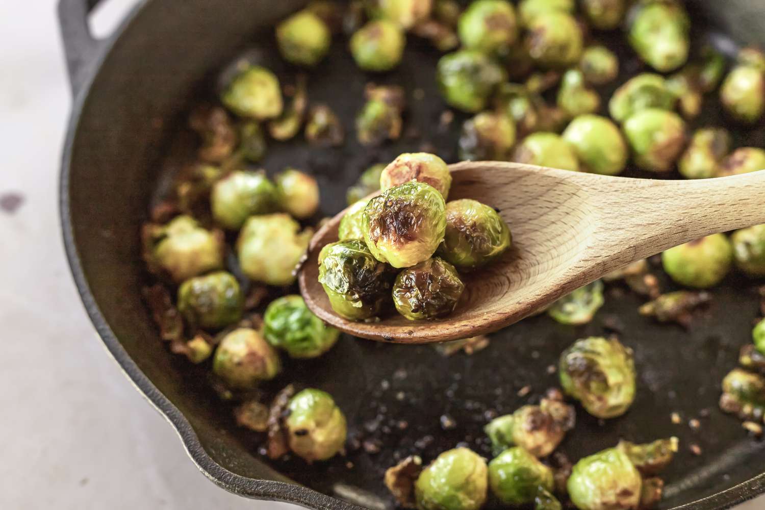 A wooden spoon scooping up roasted brussel sprouts in a cast iron pan.