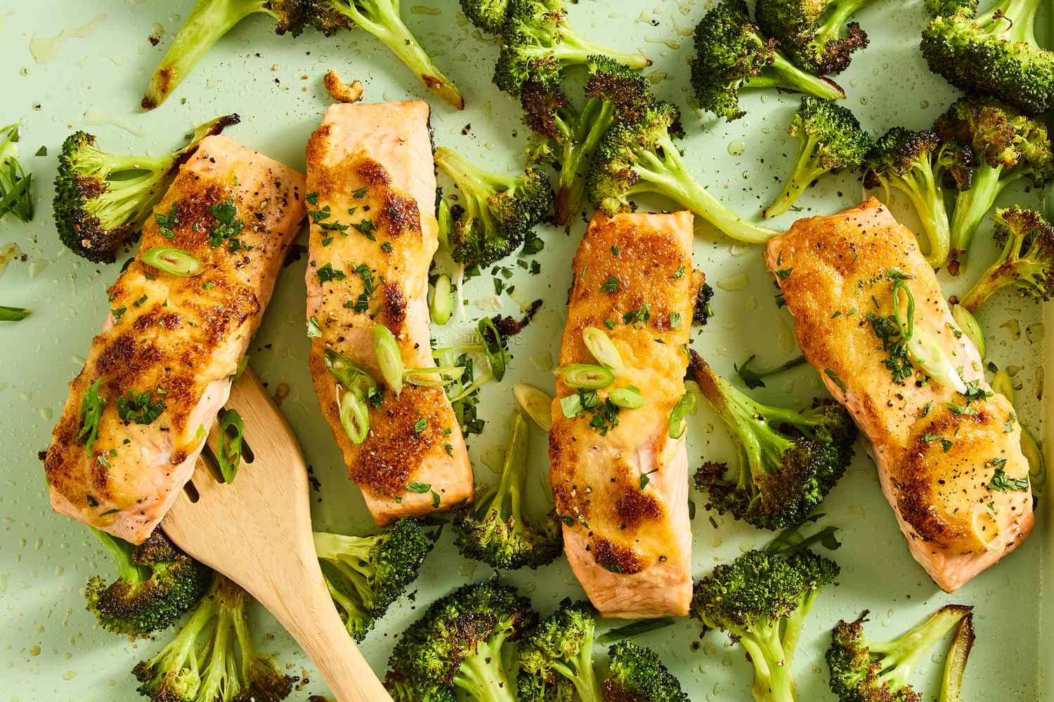 Roasted salmon fillets and broccoli on a tray with a wooden spatula