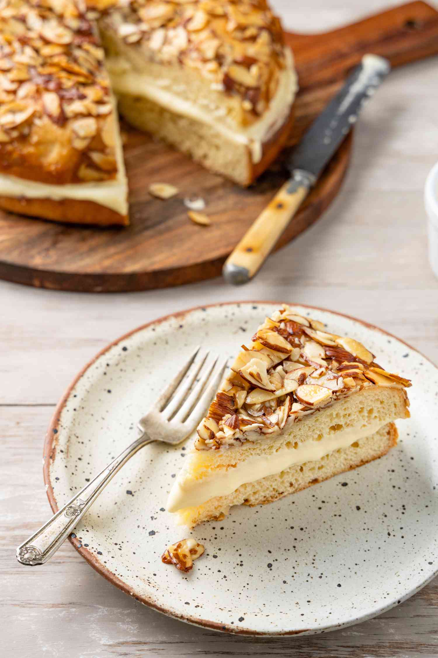 Slice of Bee Sting Cake on a Plate with a Fork with the Rest in the Background on a Circular Board