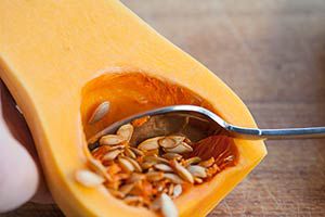 A spoon scooping out butternut squash seeds