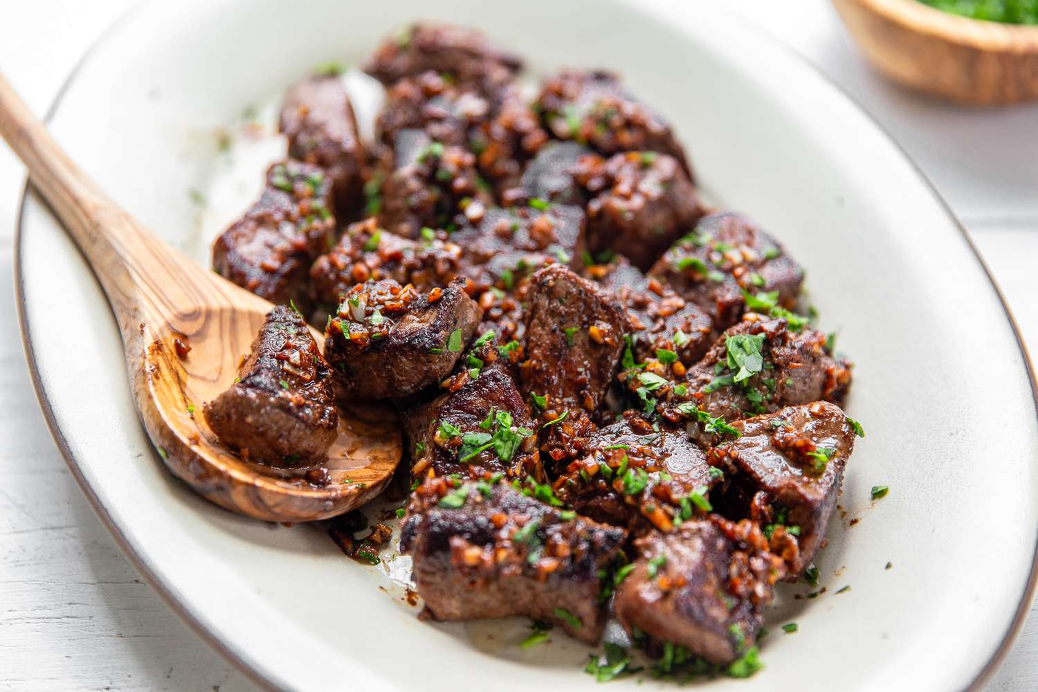 Overhead view of a white platter of Garlic Butter Steak Bites along with a wooden spoon