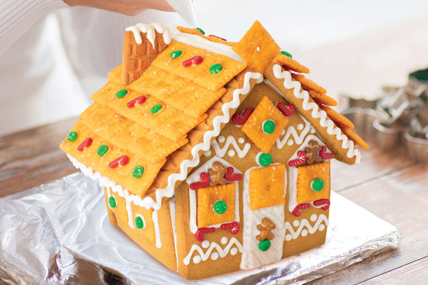 A gingerbread house decorated with crackers icing and candy on a foilwrapped base