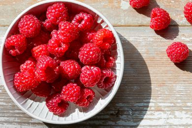 Overhead shot of a bowl of fresh raspberries on a wooden counter