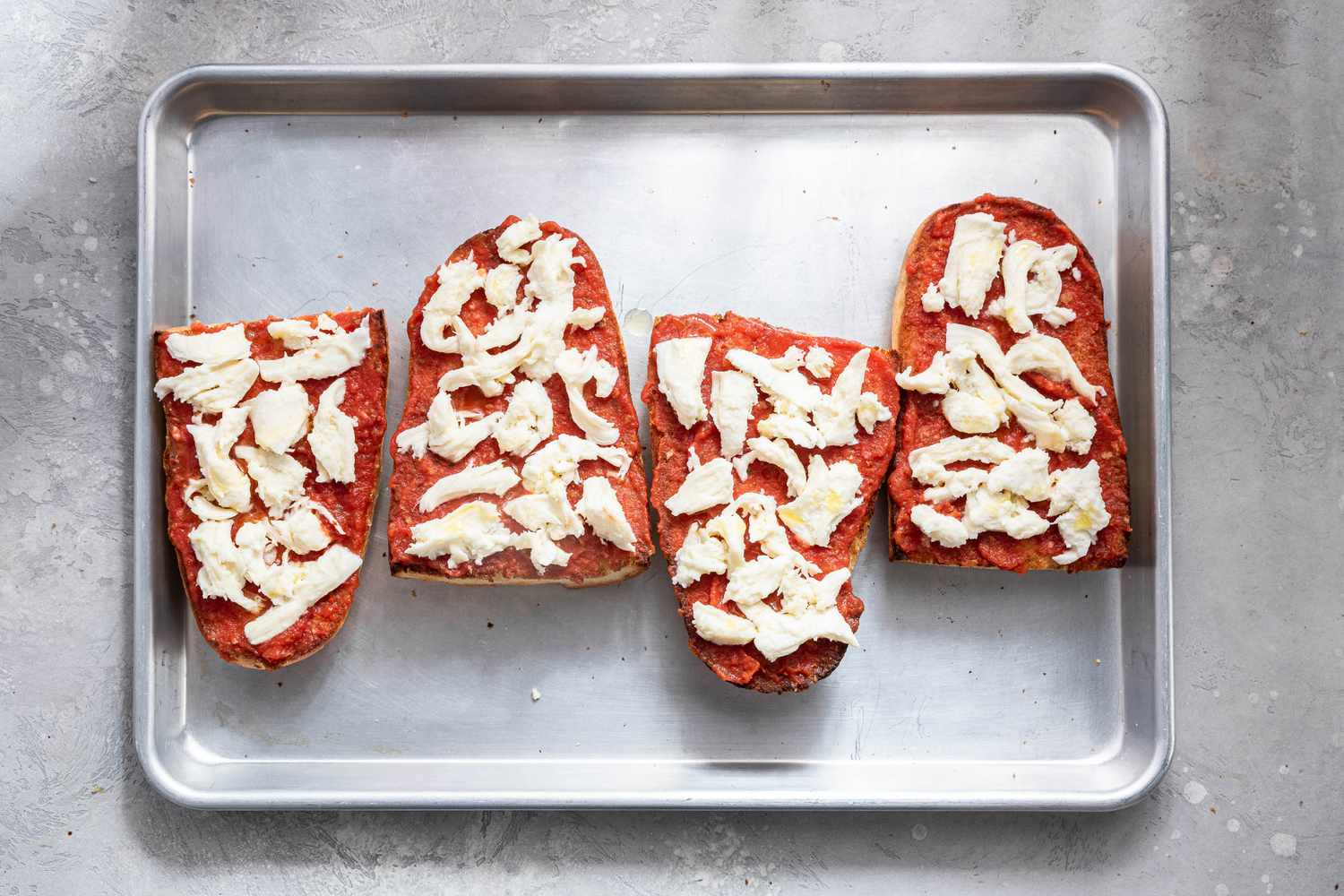 Sliced Mozzarella Added to the French Bread Pizza Quarters on the Baking Sheet 