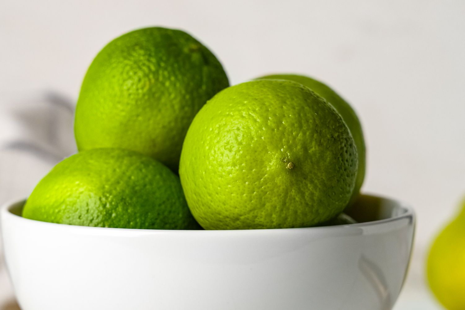 A white bowl containing several limes