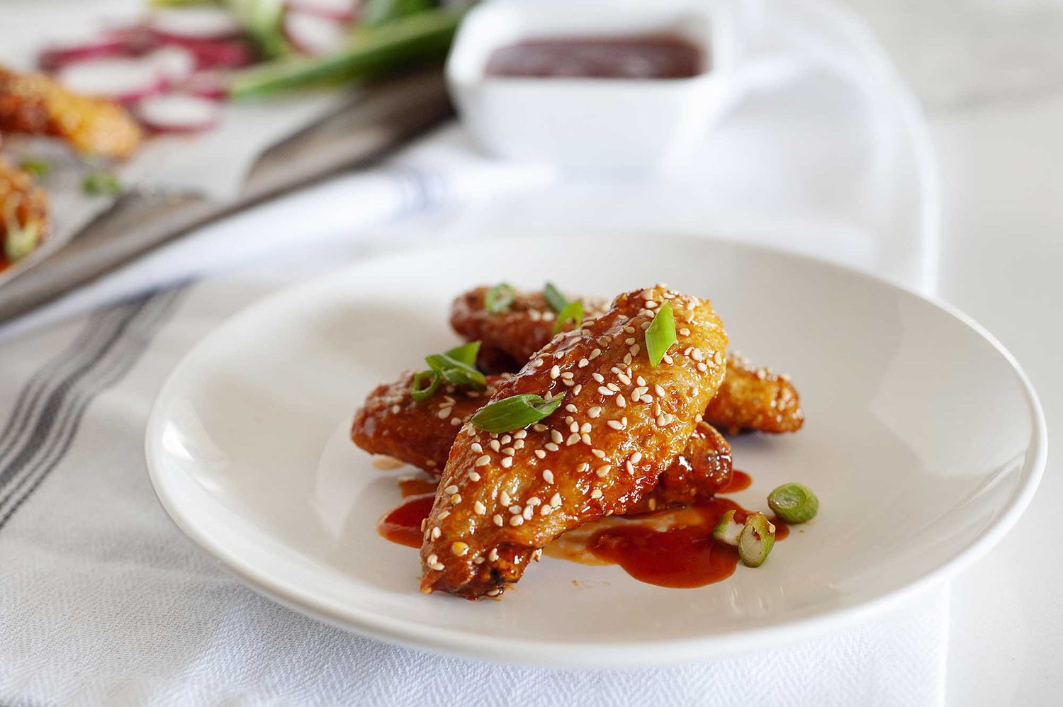 Air Fryer Chicken Wings with Gochujang Sauce and Sesame Mayo dip on a white plate sprinkled with scallions and sesame seeds.