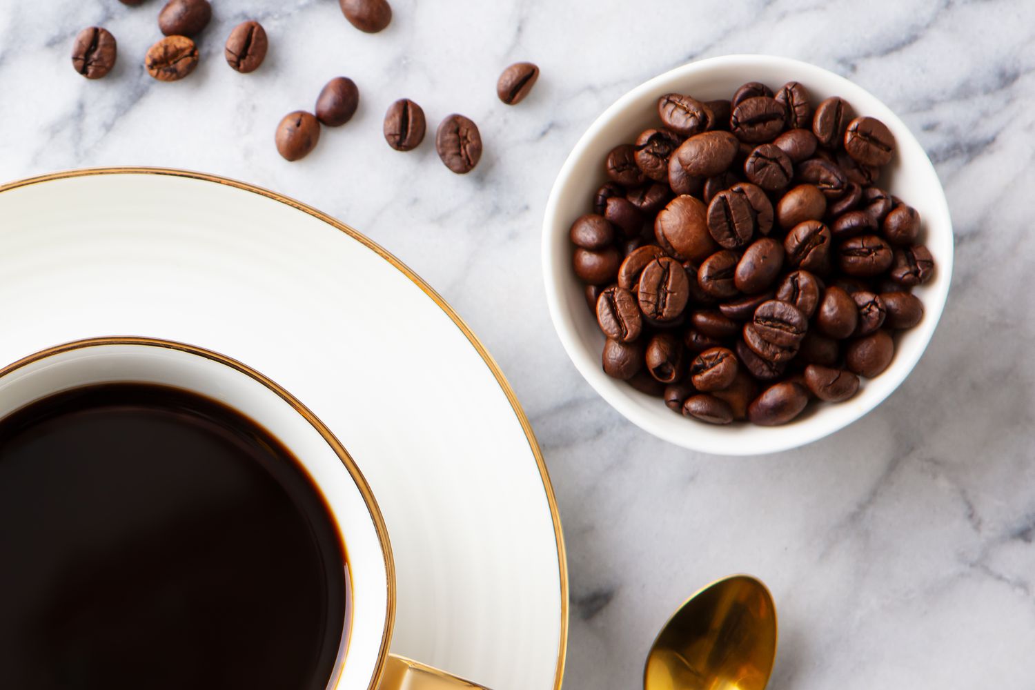 A cup of coffee with a small bowl of coffee beans next to it on a marble counter top
