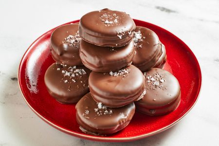 Stack of chocolatecoated cookies on a red plate sprinkled with a topping