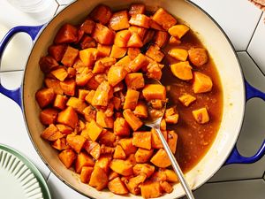 A pot of candied yams with a serving spoon viewed from above on a tiled surface with plate edges visible to the side
