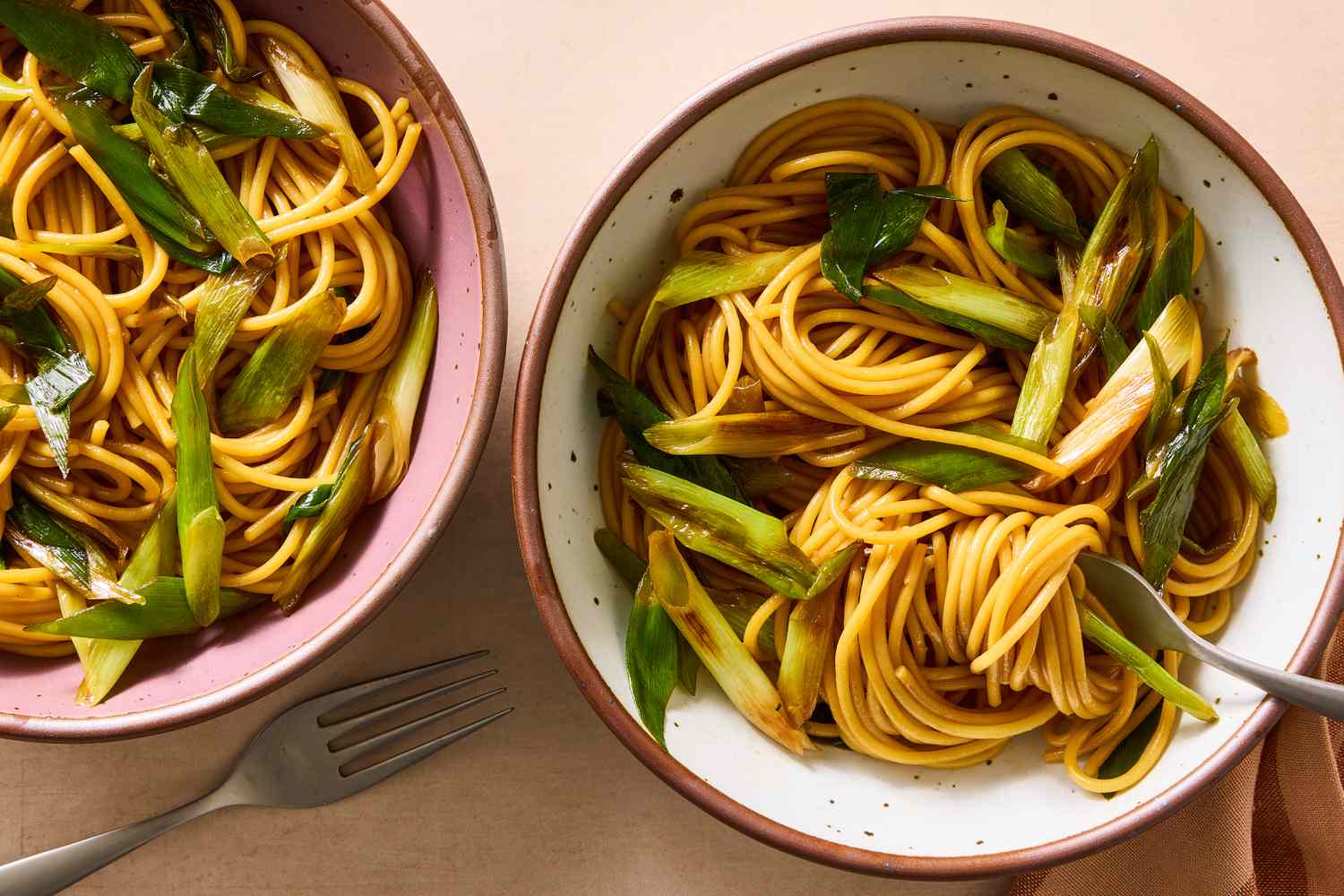Two bowls of scallion pasta on a table, with forks nearby