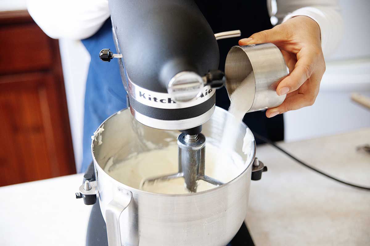 Woman adding sugar to cream cheese to make the best creme brulee cheesecake.