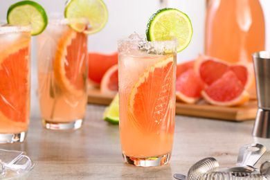 Paloma cocktail in a highbakk glass with a lime wheel garnish and cocktail ingredients in the background