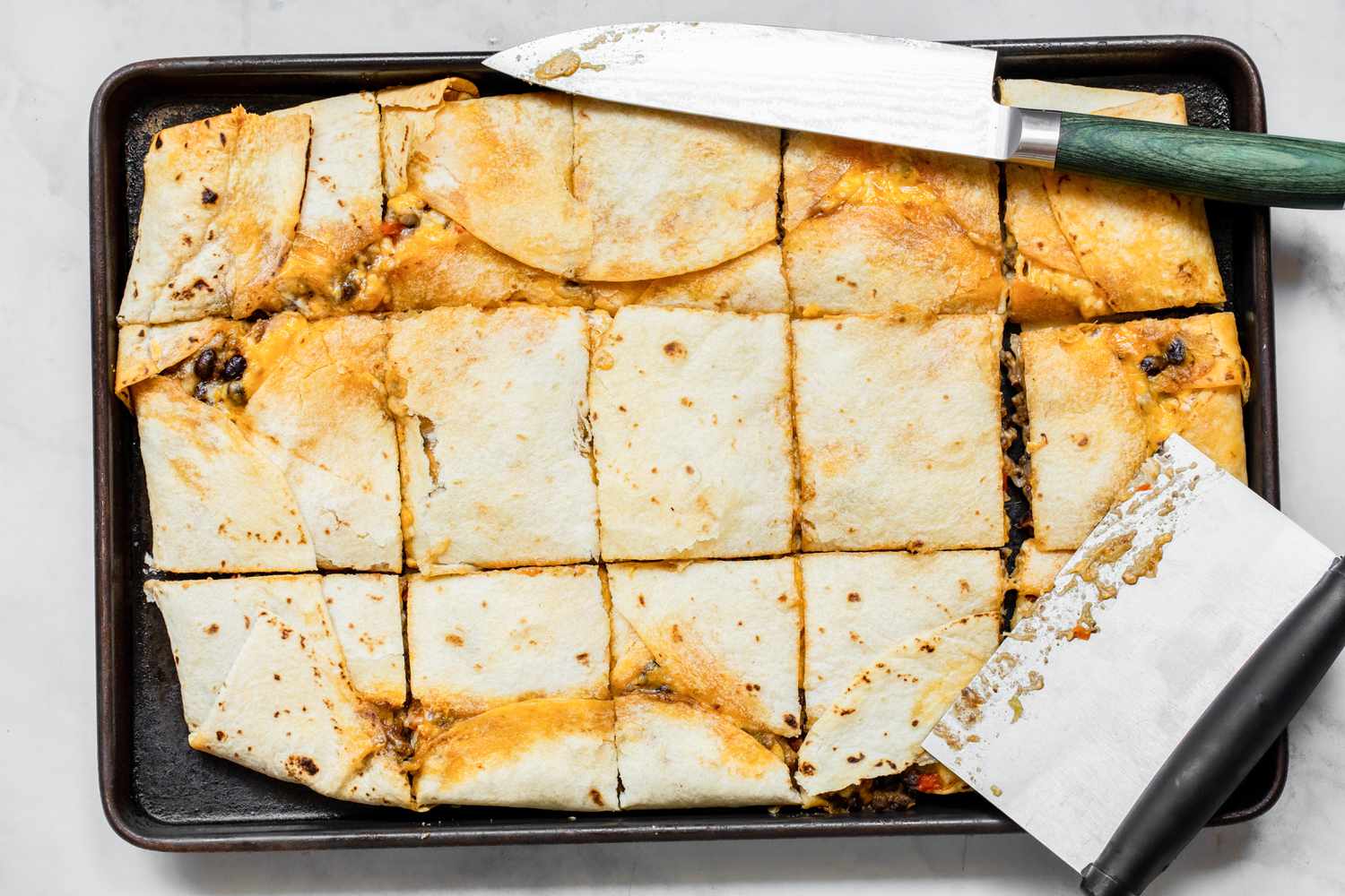 Loaded Sheet Pan Quesadillas Cut into Pieces Using a Knife and Bench Scraper
