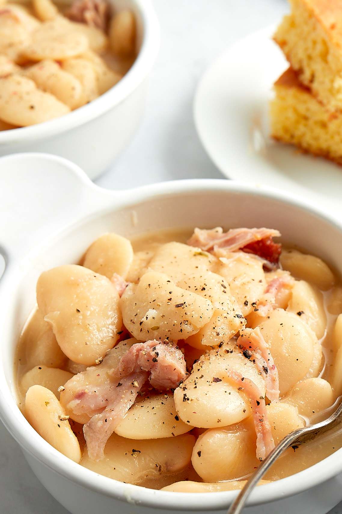 Creamy Southern Lima Beans in a Bowl with Another Bowl of Beans and a Plate of Corn Bread in the Background